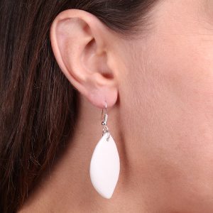 Boucle d’oreille pendante en forme de feuille, en porcelaine blanche, portée à l’oreille d’une femme aux cheveux bruns.
