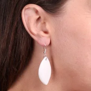 Boucle d’oreille pendante en forme de feuille, en porcelaine blanche, portée à l’oreille d’une femme aux cheveux bruns.