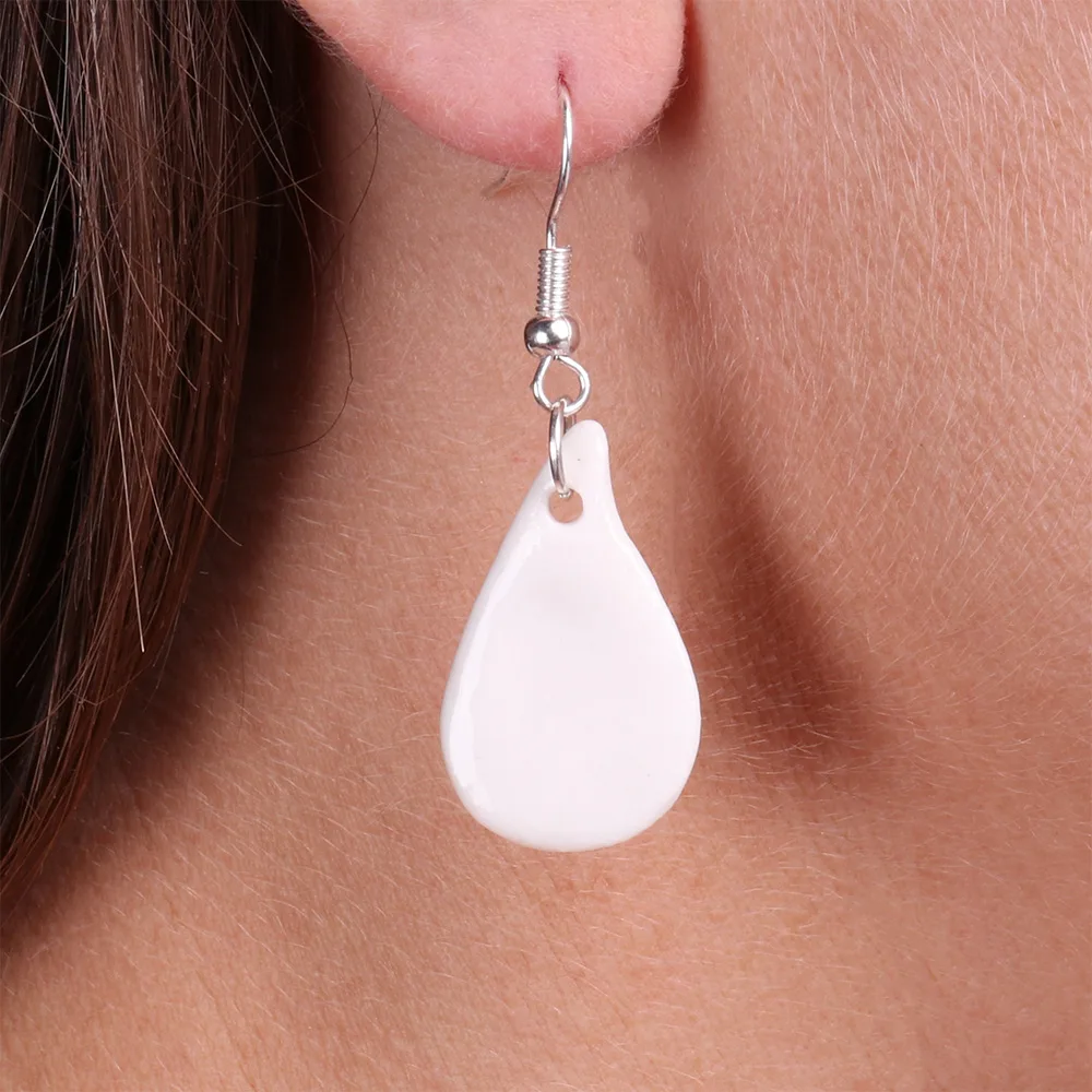 Zoom sur les boucles d’oreilles goutte en porcelaine blanche, mettant en valeur les détails de la matière artisanale.