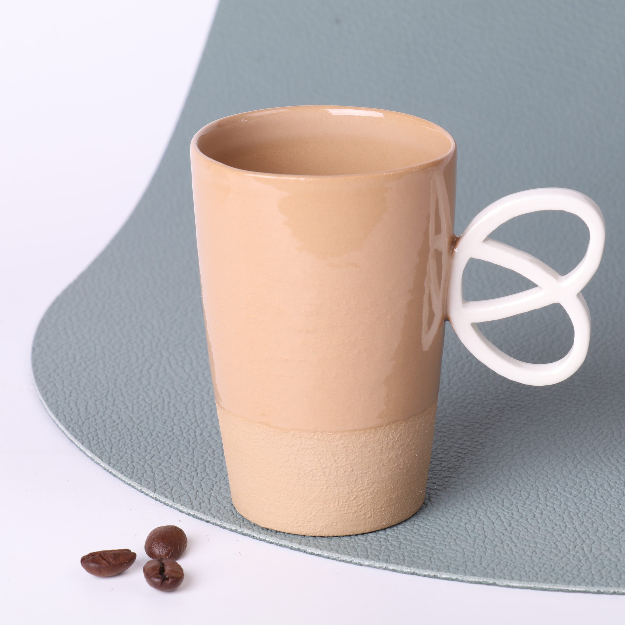 Tasse expresso artisanale – détail anse Bretzel Détail de l’anse Bretzel en porcelaine sur tasse expresso en grès caramel 90 ml, faite main en Alsace.