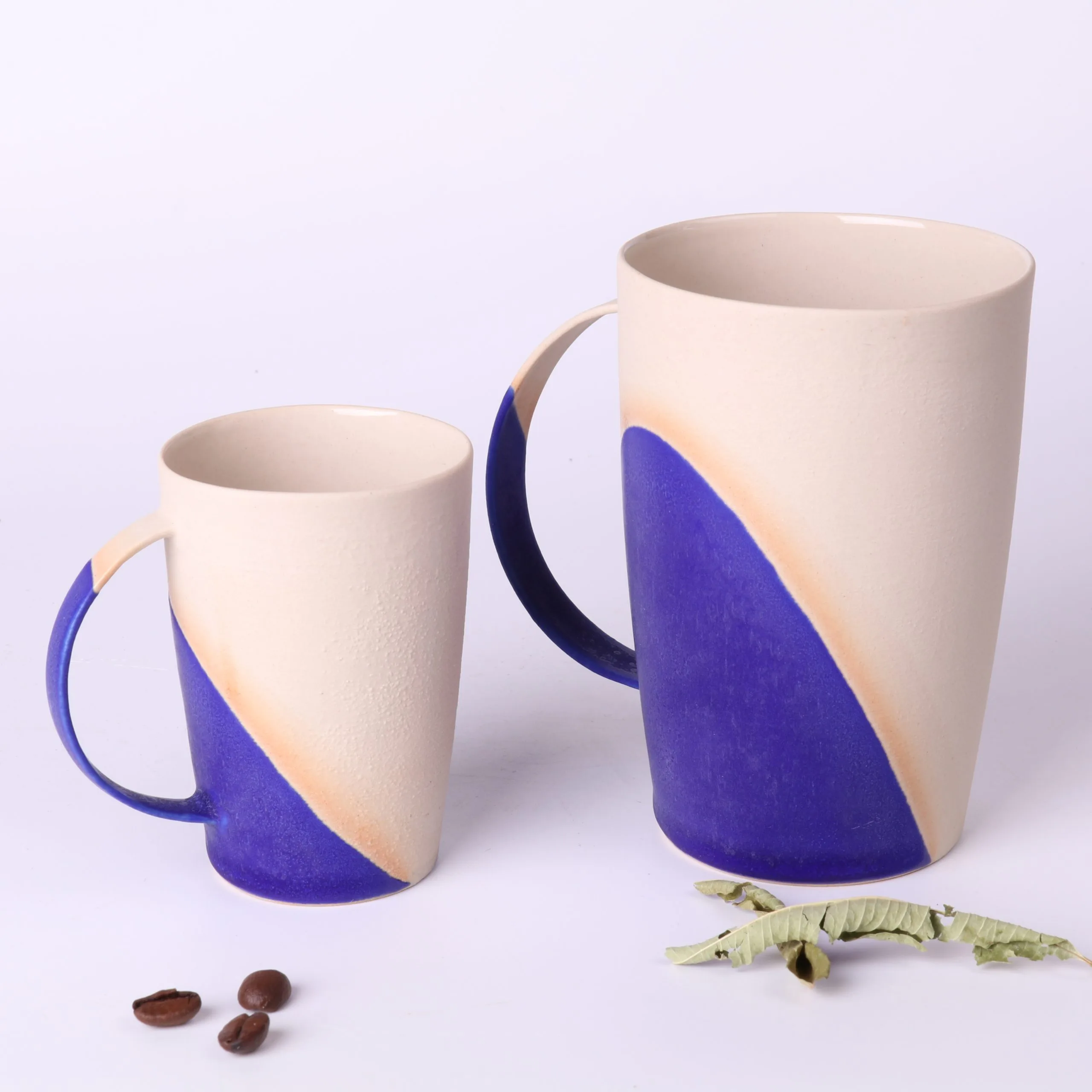 mug-poterie-artisanale-bleu-klein-330ml-et-tasse-expresso-90ml Comparatif de taille : Mug poterie artisanale Bleu Klein 330 ml et tasse expresso design 90 ml en grès, côte à côte, avec grains de café et feuilles de verveine.